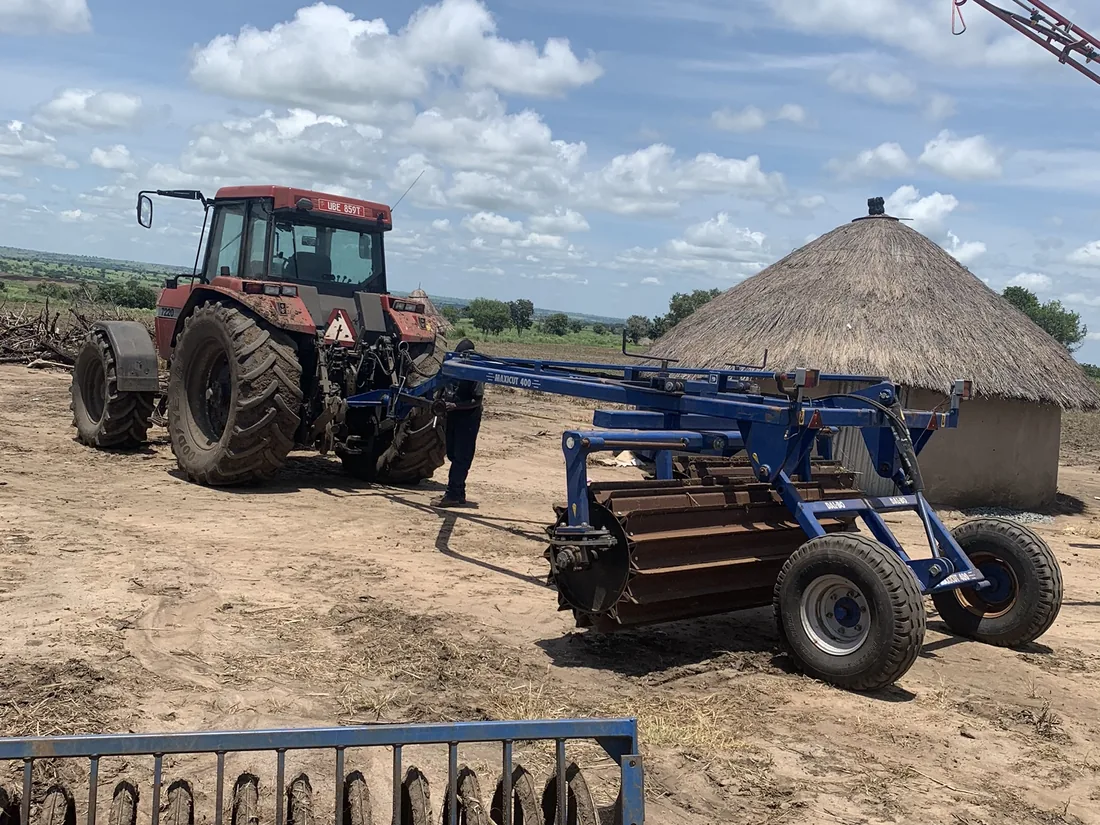 Farm equipment and staff housing at Normah's Amuru farm, with a tractor and implement in the yard.
