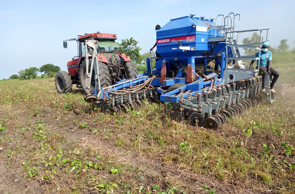 A tractor pulling a precision planter across a field, with a farmhand riding the rig, at Normah Agro Farm.